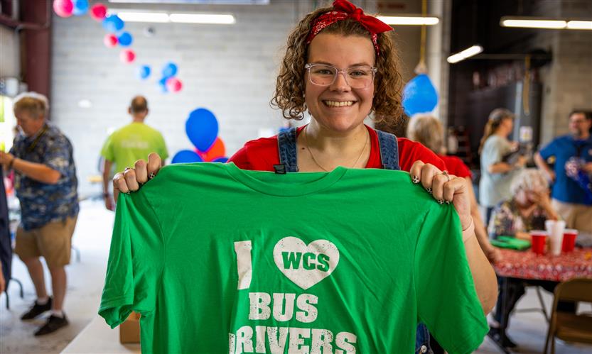 A woman with brown hair holds a green shirt reading \